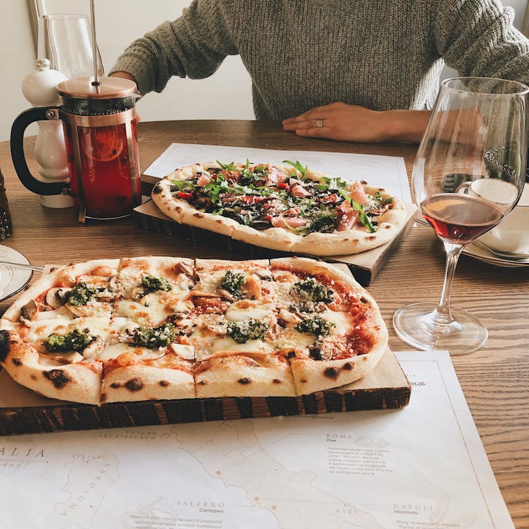 A cozy table setting with gourmet pizzas, wine, and a french press in a rustic atmosphere.